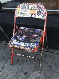 a colorful chair sitting on the sidewalk next to a store front window with graffiti all over it