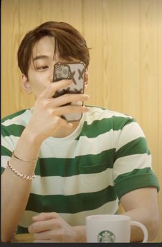 a man sitting at a table taking a photo with his cell phone while holding a coffee mug