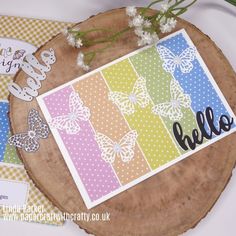 a card with butterflies and the word hello written in black on it, sitting on top of a wooden slice