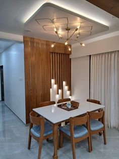 a dining room table and chairs with lights on the ceiling above it, in front of a wooden paneled wall