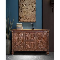 an ornate wooden cabinet in front of a blue wall with a painting on the wall