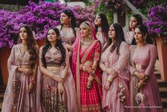 a group of women standing next to each other in front of purple flowers and bushes