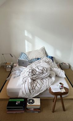 an unmade bed sitting in a bedroom next to a table with books on it