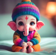 a small toy elephant wearing a multicolored hat and sweater sitting on a bed