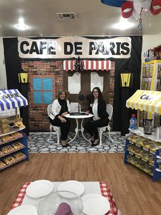 two women sitting at a table in front of a sign that says cafe de paris