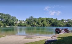 there is a wooden bridge over the water in this park area with green grass and trees on both sides