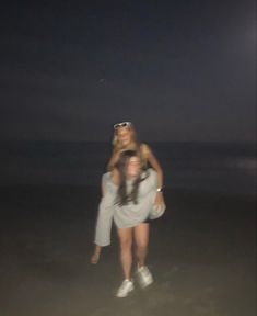 two women are standing on the beach at night with their arms around each other and one is carrying another woman