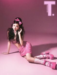 a woman sitting on the ground with her legs crossed wearing pink shoes and holding a cell phone to her ear