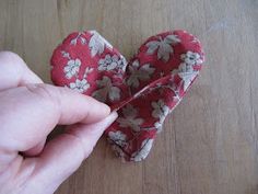 someone is holding two small hearts on a wooden table with one being stitched together