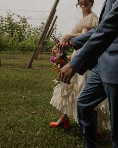 a bride and groom hold hands as they walk through the grass