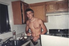 a shirtless man standing in a kitchen next to a sink