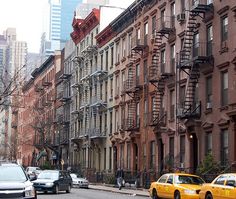 several cars are parked on the street in front of tall buildings with fire escape ladders