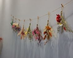 flowers are hanging on a string in front of a white wall and some feathers hang from it