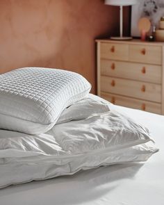 two pillows are on top of each other on a bed with white sheets and pillowcases