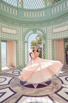 a woman in a pink dress is posing for a photo inside an ornate building with columns and arches