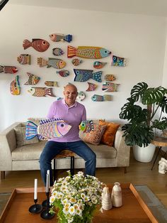 a man sitting on a couch in front of a table with flowers and vases