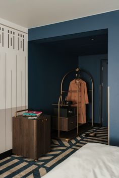 a bedroom with blue walls and white bedding has a coat on the rack next to it