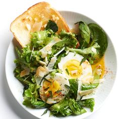 a white plate topped with a salad and an egg on top of toasted bread