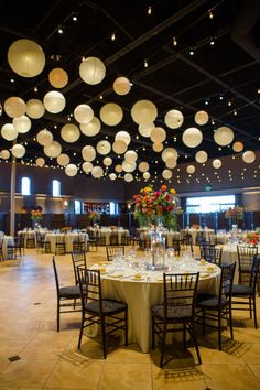 a banquet hall with round tables and hanging paper lanterns