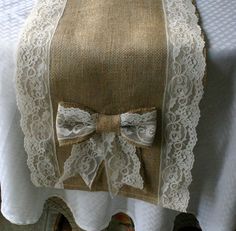 a white table cloth with a bow on it and lace around the edge, sitting on top of a dining room table