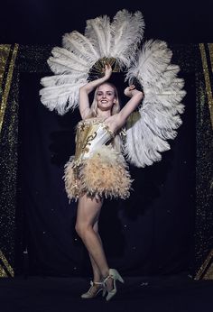 a woman in a gold and white feathered dress posing for the camera with her hands behind her head