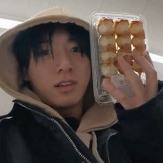 a young man holding up a plastic container filled with donuts