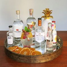 an assortment of alcohol bottles and glasses on a tray with orange slices, pineapples, gin