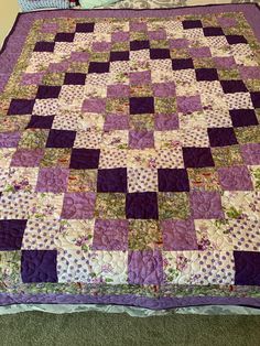 a bed with a purple and white quilt on it's headboard next to a pillow