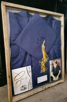 a graduation cap and gown are displayed in a wooden frame with other items around it