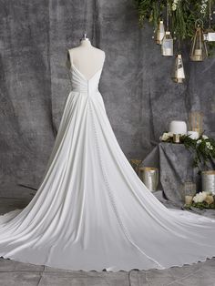 a white wedding dress on display in front of a gray backdrop with candles and flowers