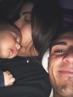 a man and woman laying next to each other with a baby sleeping on top of them