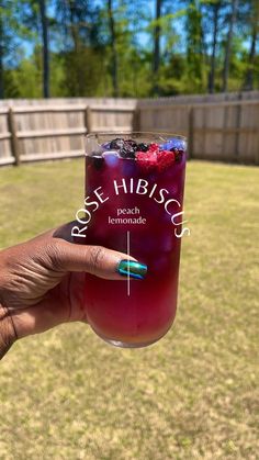 a person holding up a glass with ice and berries on it in front of a fence