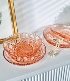 two pink glass plates sitting on top of a white table next to a gold frame