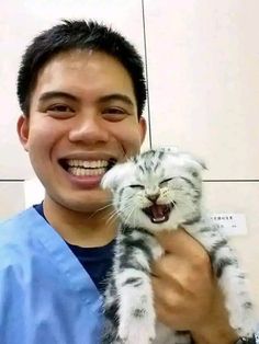 a man in scrubs holding a cat up to his face and smiling at the camera