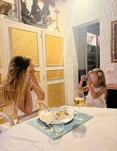 two women sitting at a table with plates of food and wine in front of them