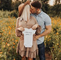 a man and woman standing in a field holding a baby's shirt