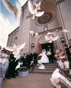 black and white photograph of wedding party in front of church with doves flying around