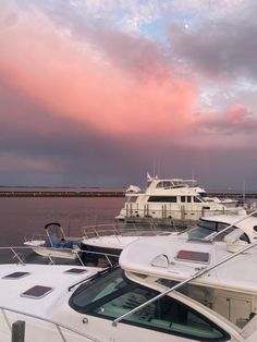 several boats are docked in the water under a pink sky with some clouds above them