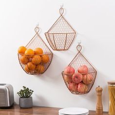 two metal baskets with fruit hanging on the wall above a wooden counter top next to a toaster and microwave