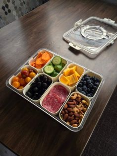 a plastic container filled with assorted fruits and veggies on top of a wooden table