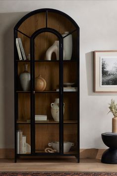 An Image of the 4 -Tier Modern Standing Arched Display Cabinet with Glass Doors against a white painted wall, beside a wall photo and a small vase. Bedroom Glass Cabinet, Cabinet For Study Room, Arch Glass Cabinet Doors, Arched Bookshelf With Doors, Display Cabinet Ideas, Bookshelf With Glass Doors, Arched Display Cabinet, Modern Display Cabinet, House Accents