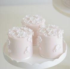 three small pink cakes sitting on top of a white cake stand