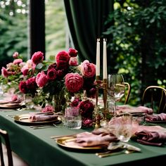 the table is set with pink flowers and gold place settings, candles and napkins