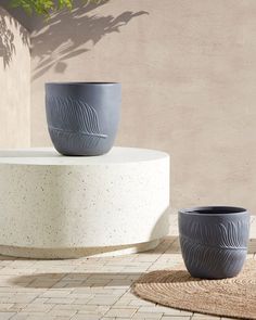 two grey planters sitting on top of a white table