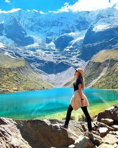 a woman standing on top of a mountain next to a lake