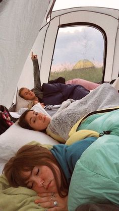 two women laying on a bed in a tent while one woman lays down next to her