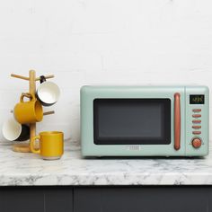 a microwave oven sitting on top of a counter next to two mugs and a rack