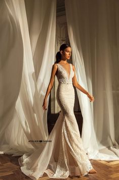 a woman in a wedding dress standing on a wooden floor with white curtains behind her