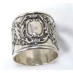 a silver ring with an initial on the front and initials on the back, sitting on a white surface