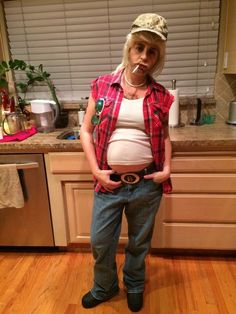 a pregnant woman standing in a kitchen with her belly exposed and wearing a hat on top of her head